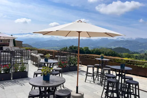 Rooftop patio with black, circular chairs and tables, looking out towards an open valley