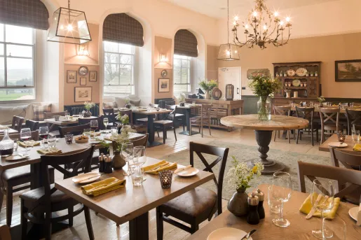 Dining hall with wooden tables and leather chairs, with large windows on the left