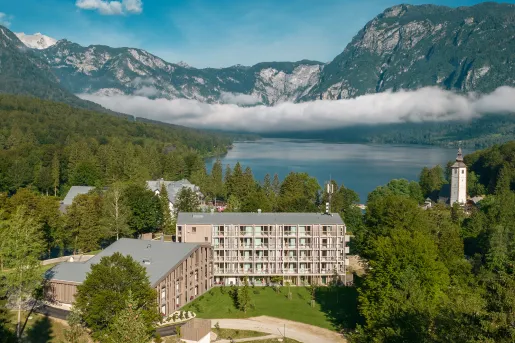 Exterior sky view of a large wooden hotel building with a large lake and mountains in the background