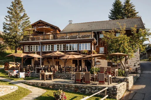 Exterior view of wooden hotel lodge with large umbrellas and dining tables outside