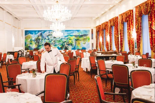 Dining hall with a waiter arranging red chairs around circular white tables