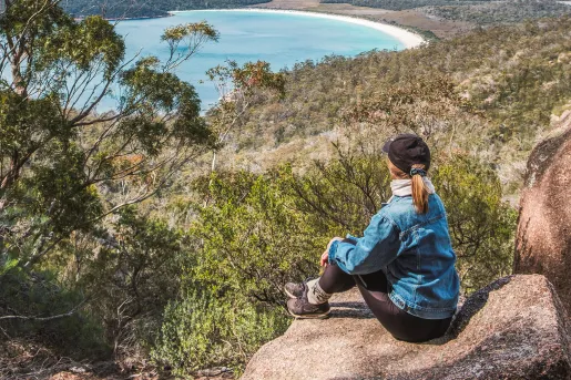 Woman sitting on a boulder, looking out to a large valley and a lake