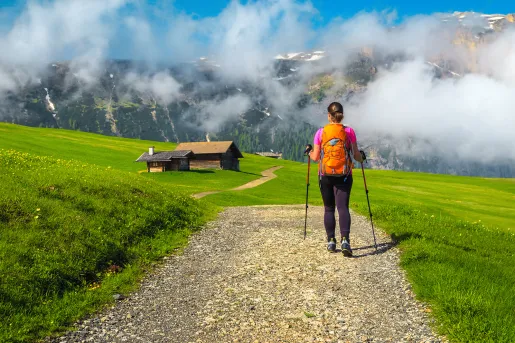 Woman with walking poles, trekking through a grassy valley