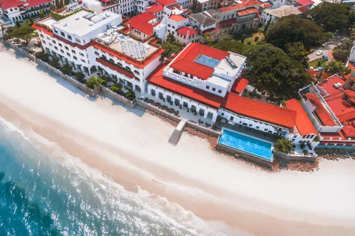 Sky view of large, white hotel complex with red roofing and the beach in front