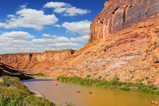 Large river next to a canyon, with people in red rafts paddling through the river