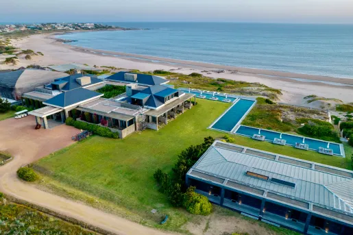 Sky view of two large hotel buildings with a grass field and outdoor pool, with the ocean in the background