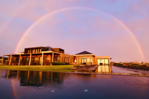 Hotel complex with a large pool in front, with a rainbow in the sky