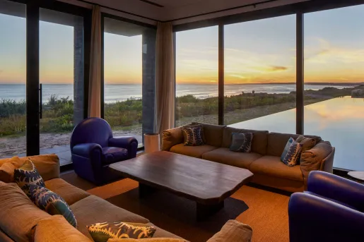 Corner area of a room with large windows, and two couches surrounding a wooden table