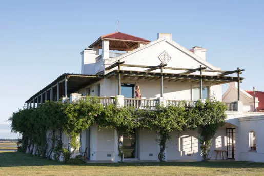 Exterior view of large, white building with two floors and branches surrounding the walls