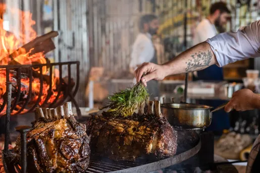 Person sprinkling rosemary on large slabs of meat on a grill