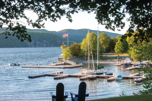 Two small, wooden chairs on a field of grass, overlooking a lake docked with boats