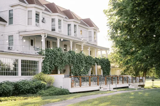 Exterior view of two-story, white house with large bushes and chairs in front