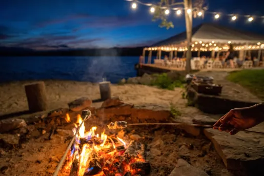 Outdoor firepit by the beach, with people roasting marshmallows on sticks