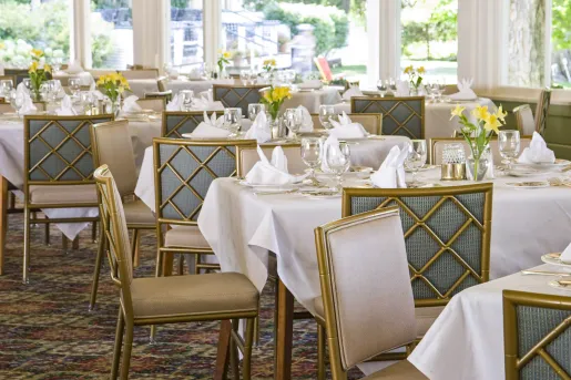 Restaurant dining hall with gold chairs and tables with white cloths on top