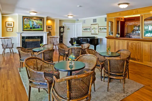 Bar and lounge with wooden chairs around green, circular tables, and a piano in the background