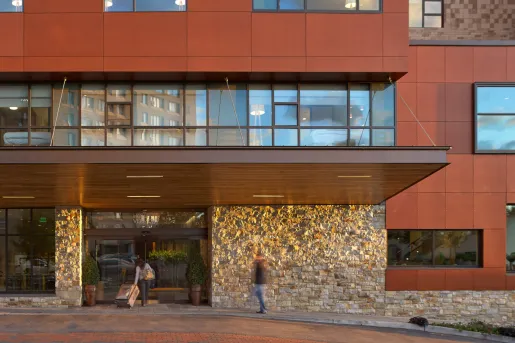 Exterior view of red building with exposed brick, and people walking in with suitcases