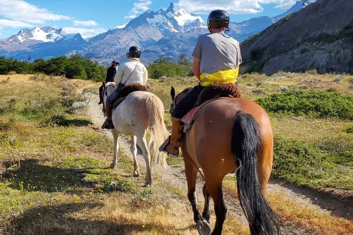 Three people horseback riding on a dirt trail in the middle of an open valley