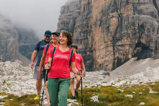 Three women and one man hiking on a grassy trail with fog-covered mountains in the background