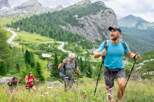 Group of men and women hiking up a grassy hill, with large valleys in the distance