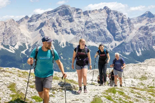 Group of men and women hiking on a rocky trail, with tall mountains in the distance