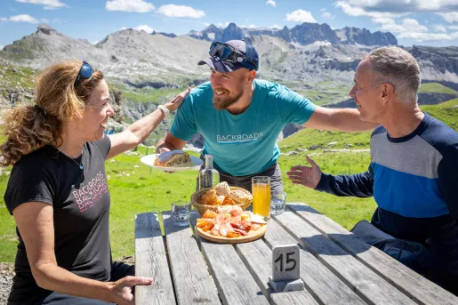 Two men and one woman smiling while being served a plate of bread and cured meats