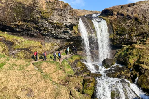 Group of people hiking on a hill with a waterfall over the hill