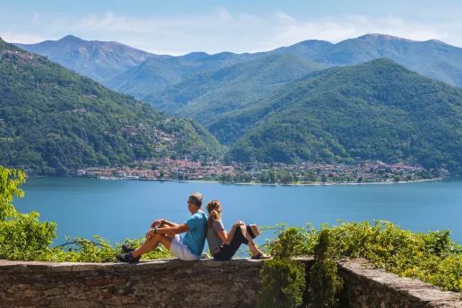 Man and woman sitting on a brick wall, looking out to a lake and a town in the distance