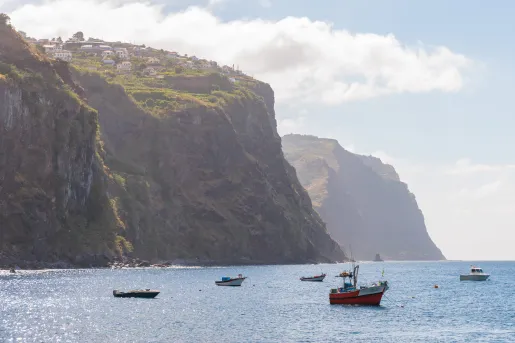 Boats floating in the ocean, with a large cliff with houses in the background