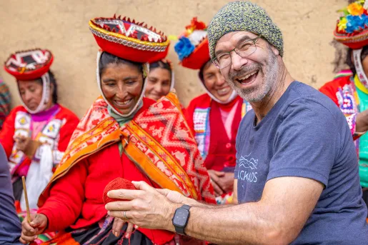 Man smiling while holding a ball of yarn, next to a woman wearing traditional attire