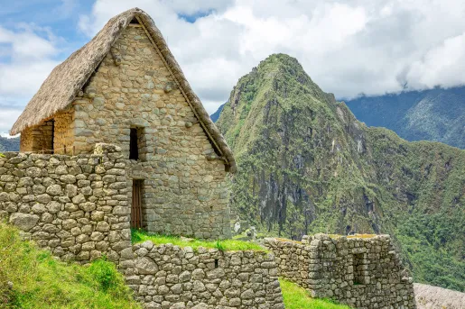 Rustic, stone buildings on top of a dirt trail with large mountains in the background
