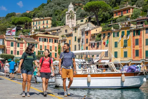 Two women and one man walking along a boat dock, with orange buildings in the background