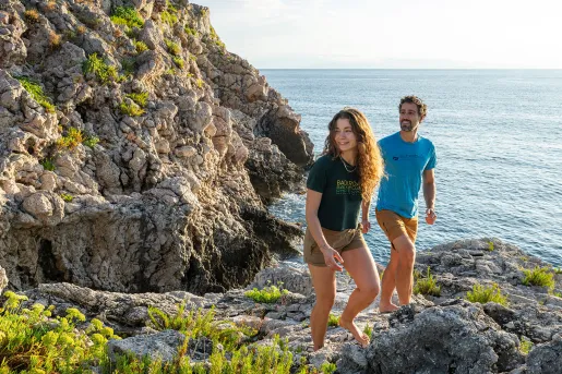 Man and woman walking on boulders next to the ocean shore