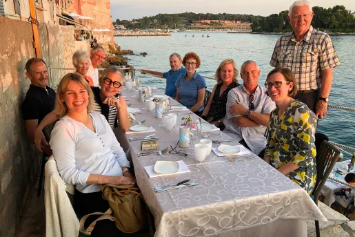Group of people smiling, sitting around a dining table by the water