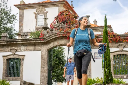 Woman smiling with two hiking poles, walking in front of a castle-like building