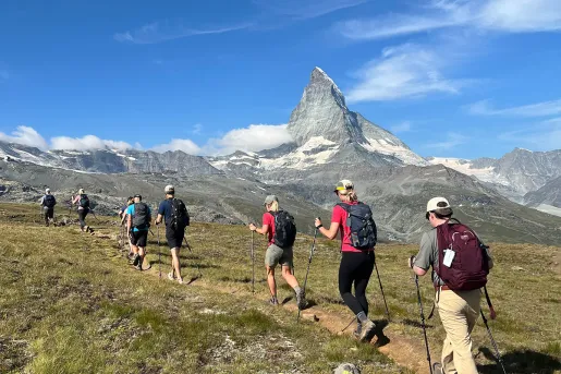 Group of people walking on a dirt trail, with large mountains in the distance