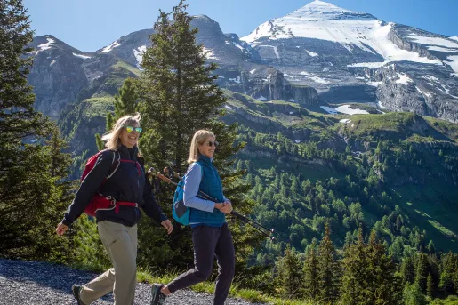 Two women hiking along a rocky trail, with snow-capped mountains in the background