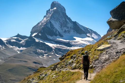 Woman using hiking poles, walking on a trail with tall mountains in front