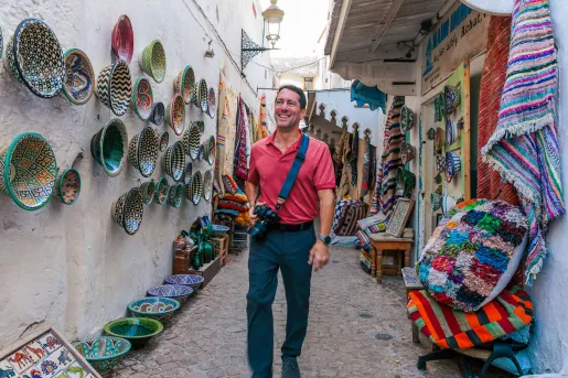 Man standing in an alleyway, surrounded by baskets and pots on the walls