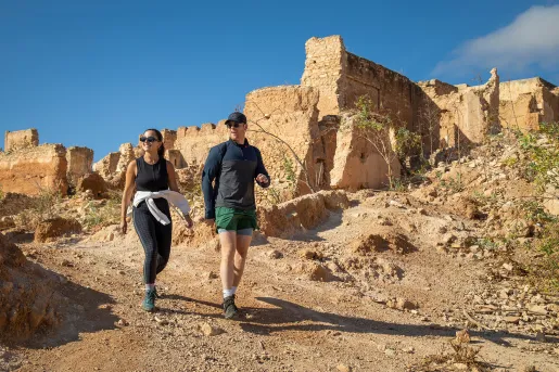 Man and woman walking on a dirt trail with ruins in the background