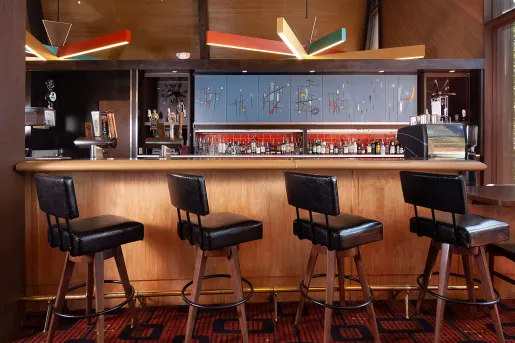 Bar and lounge with black, leather stools in front of a counter