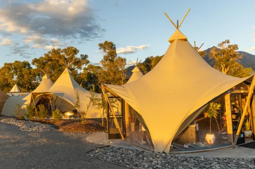 Two large, luxury tents with taller trees in the background