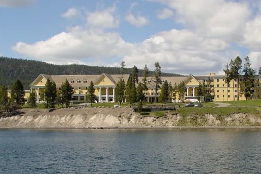 Exterior view of large, yellow building with trees and a lake in front