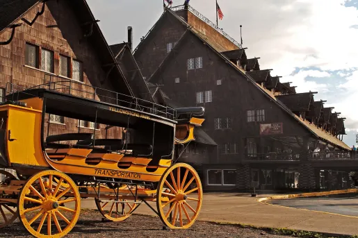 Old-style black and yellow wagon in front of a large, wooden cabin building