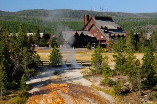 Geyser in the middle of a valley, with a large cabin in the background