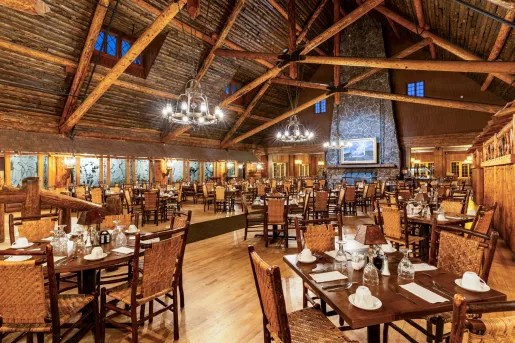 Large cabin dining hall with a large stone fireplace in the background and wooden dining tables throughout the room
