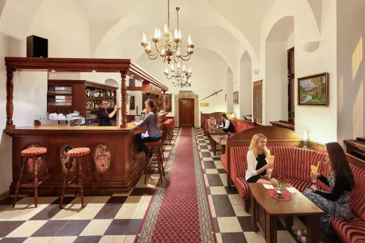 Bar and lounge with people sitting in cushioned booths, raises glasses of alcoholic beverages