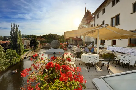 Outdoor patio and dining area in front of a white building, with a river in the distance