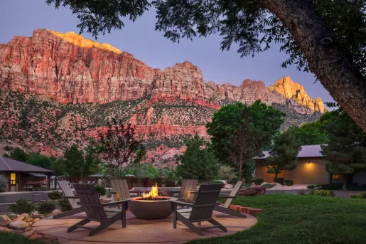 Outdoor patio with chairs surrounding a firepit with large mountains in the background