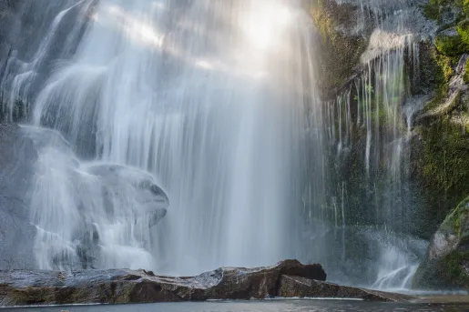 Large waterfall with a lake on the ground level, being hit by the sunlight