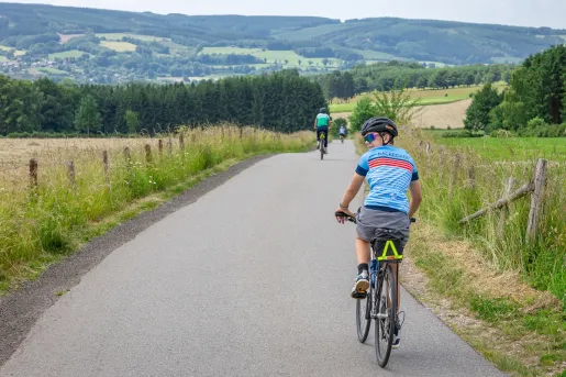 Woman biking on an empty road, with large grassy hills in the distance